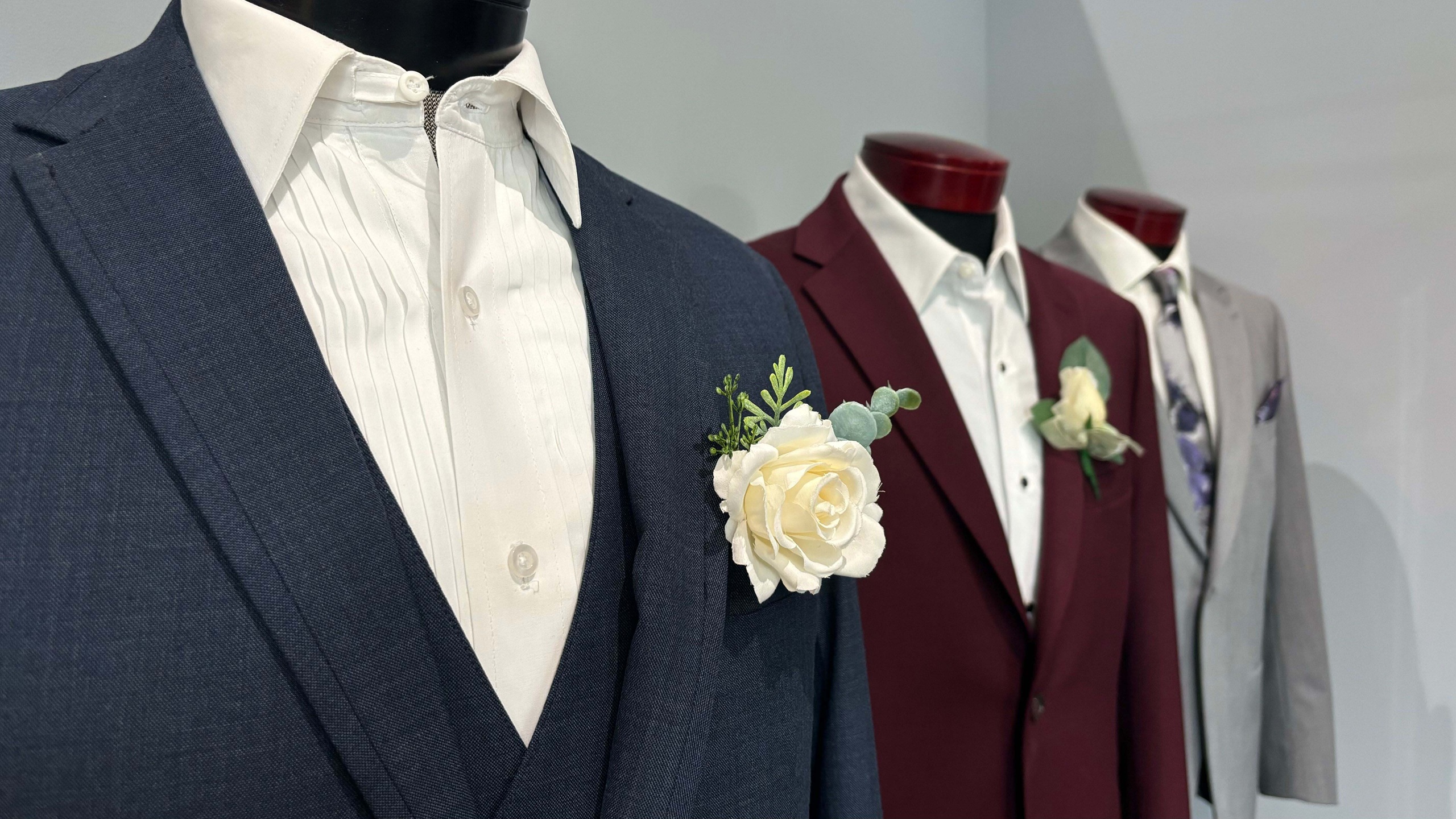 A closeup shot of 3 men's suites lined up with white flowers for each.