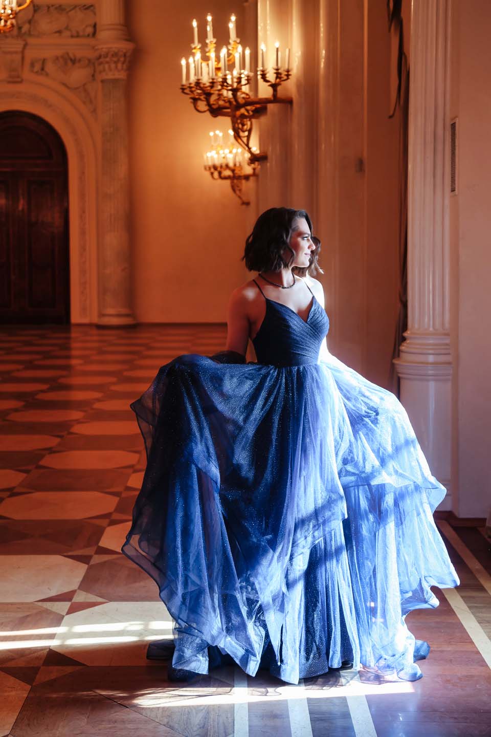 Bride in blue flowy dress looking out a window.
