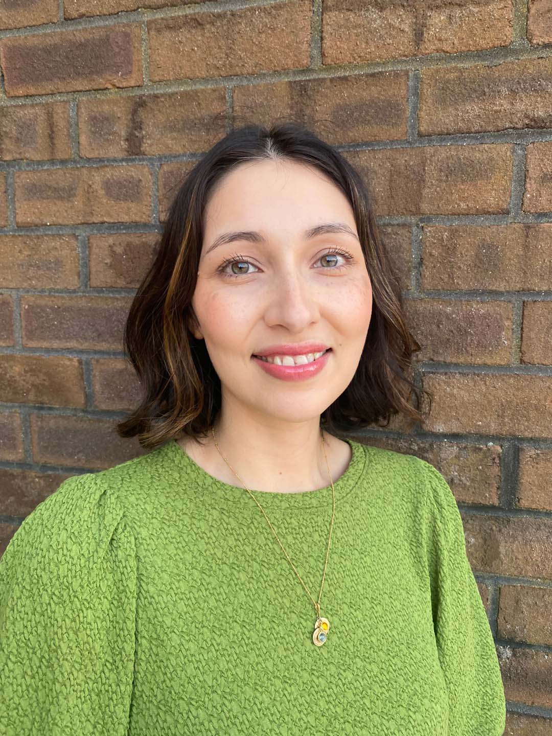 Felicia smiling in green top and gold necklace for team headshot.
