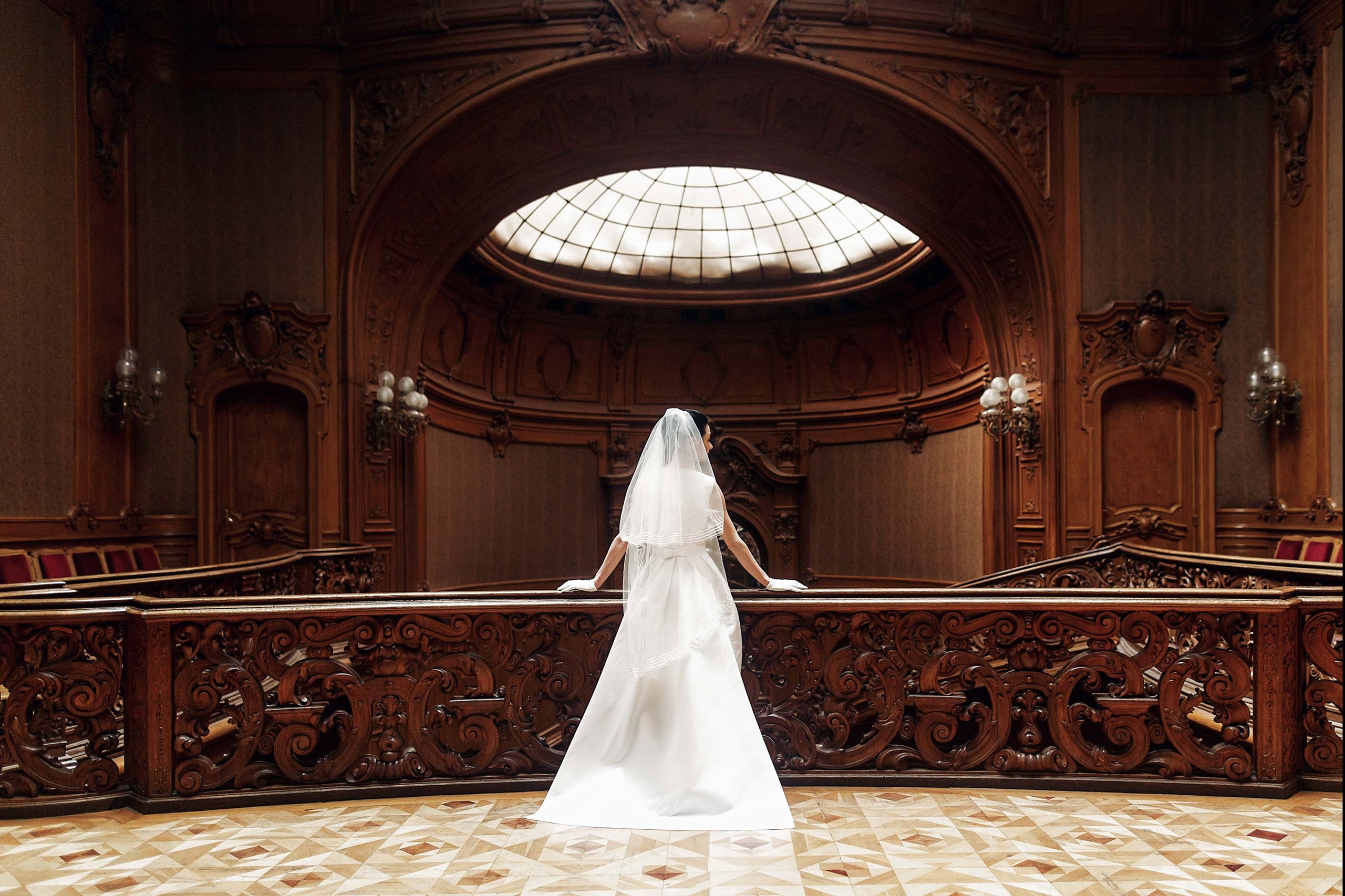 Bride in white dress with veil on standing at a balcony in a wedding venue.