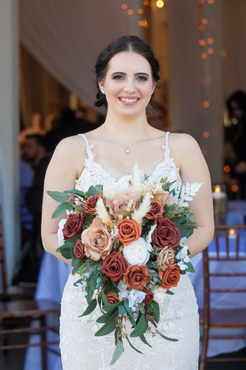 Bride holding floral arrangement in a white dress wearing a necklace.